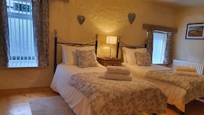 Un dormitorio con dos camas, una mesita de noche con lámpara, decoraciones en forma de corazón en la pared y una ventana con persianas.