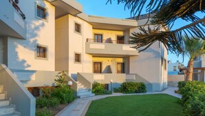 A modern two-story building with a flat roof, a small balcony, and a well-maintained lawn. - John Mary Apartments by Estia (Hersonissos)