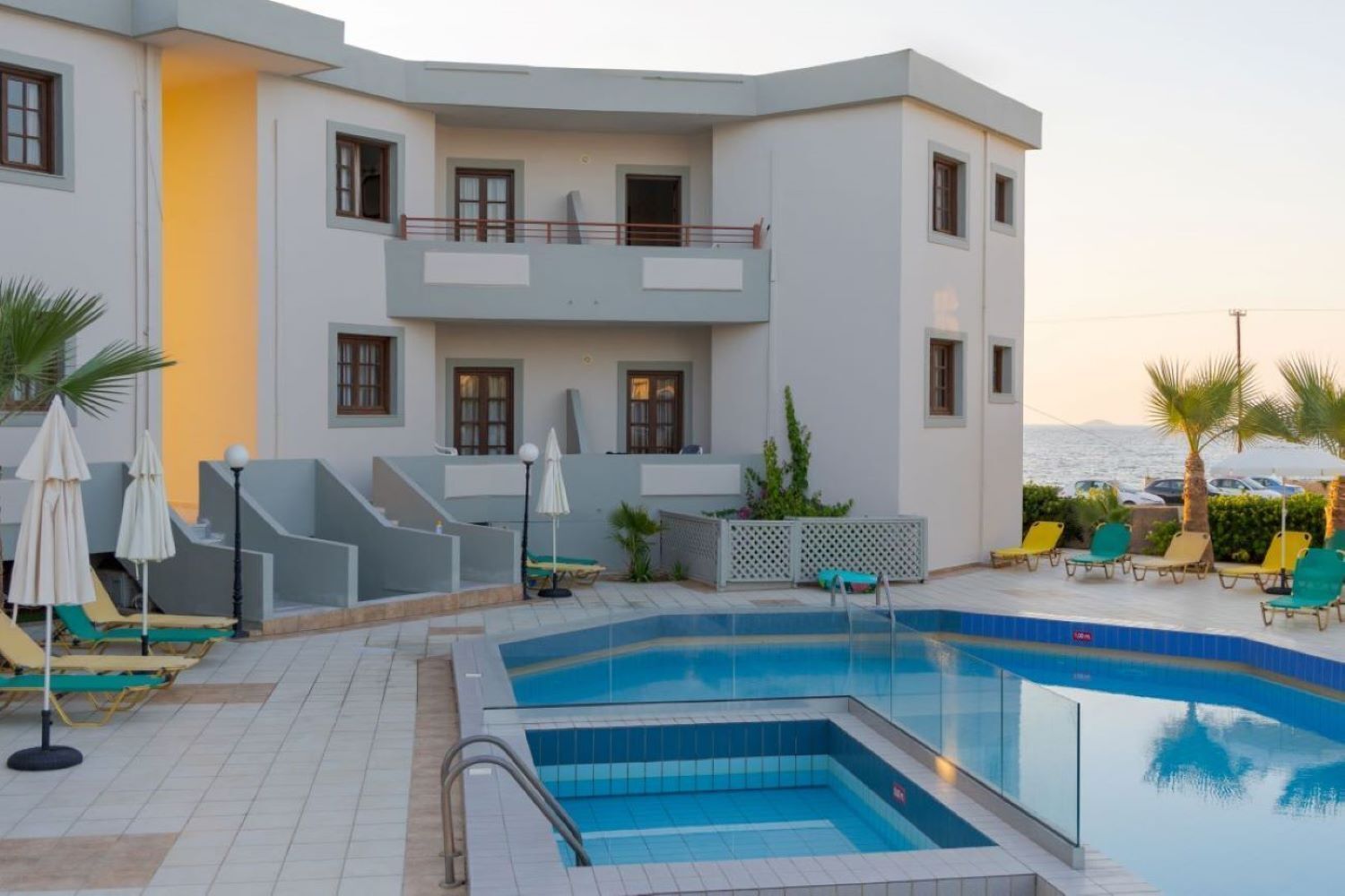 Un hotel moderno con zona de piscina, sillones de descanso y sombrillas, y vistas al mar.