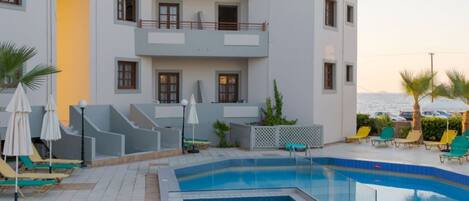 Un hotel moderno con zona de piscina, sillones de descanso y sombrillas, y vistas al mar.