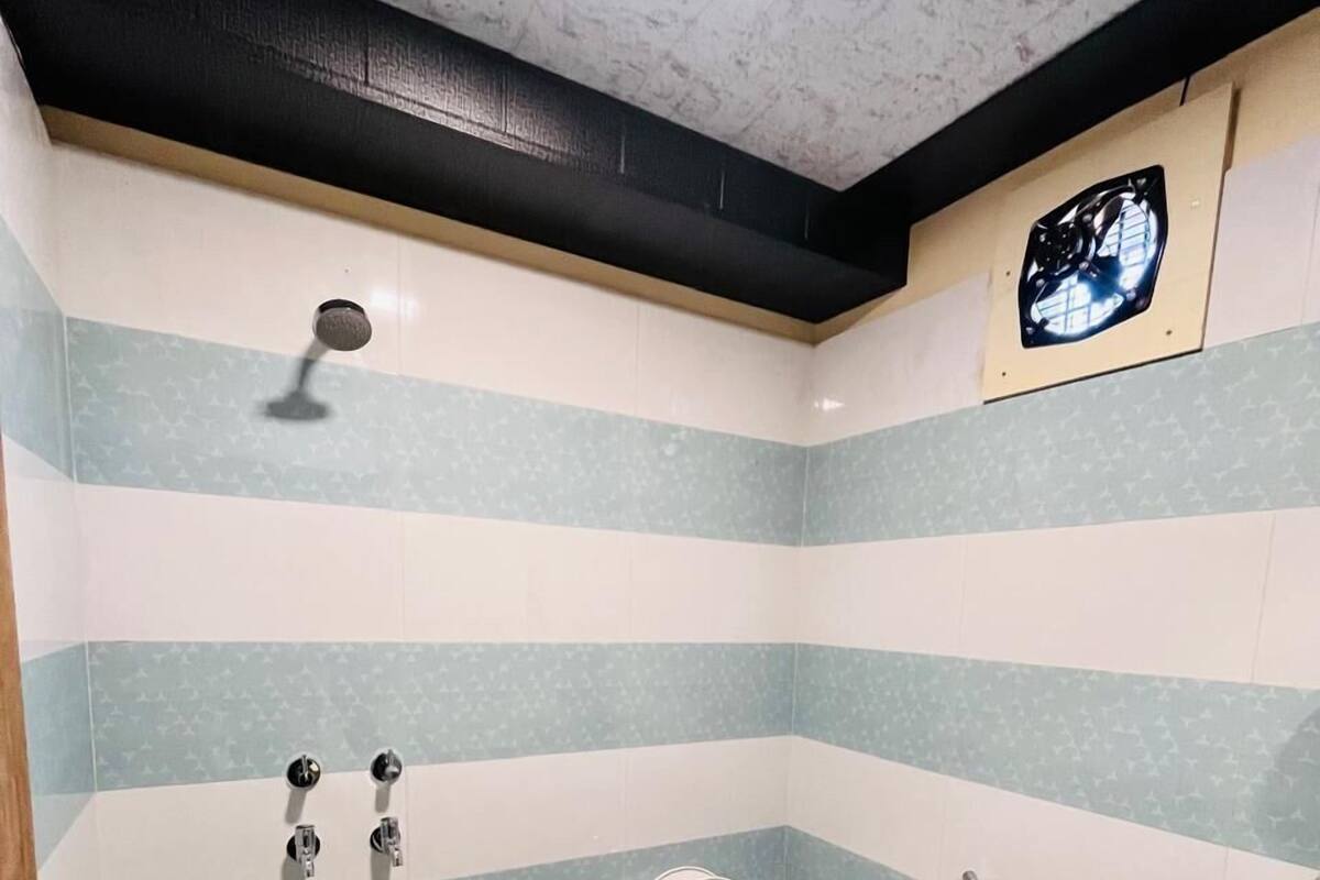 A bathroom with a toilet, bidet, and sink, featuring striped tile walls and a ceiling light fixture.