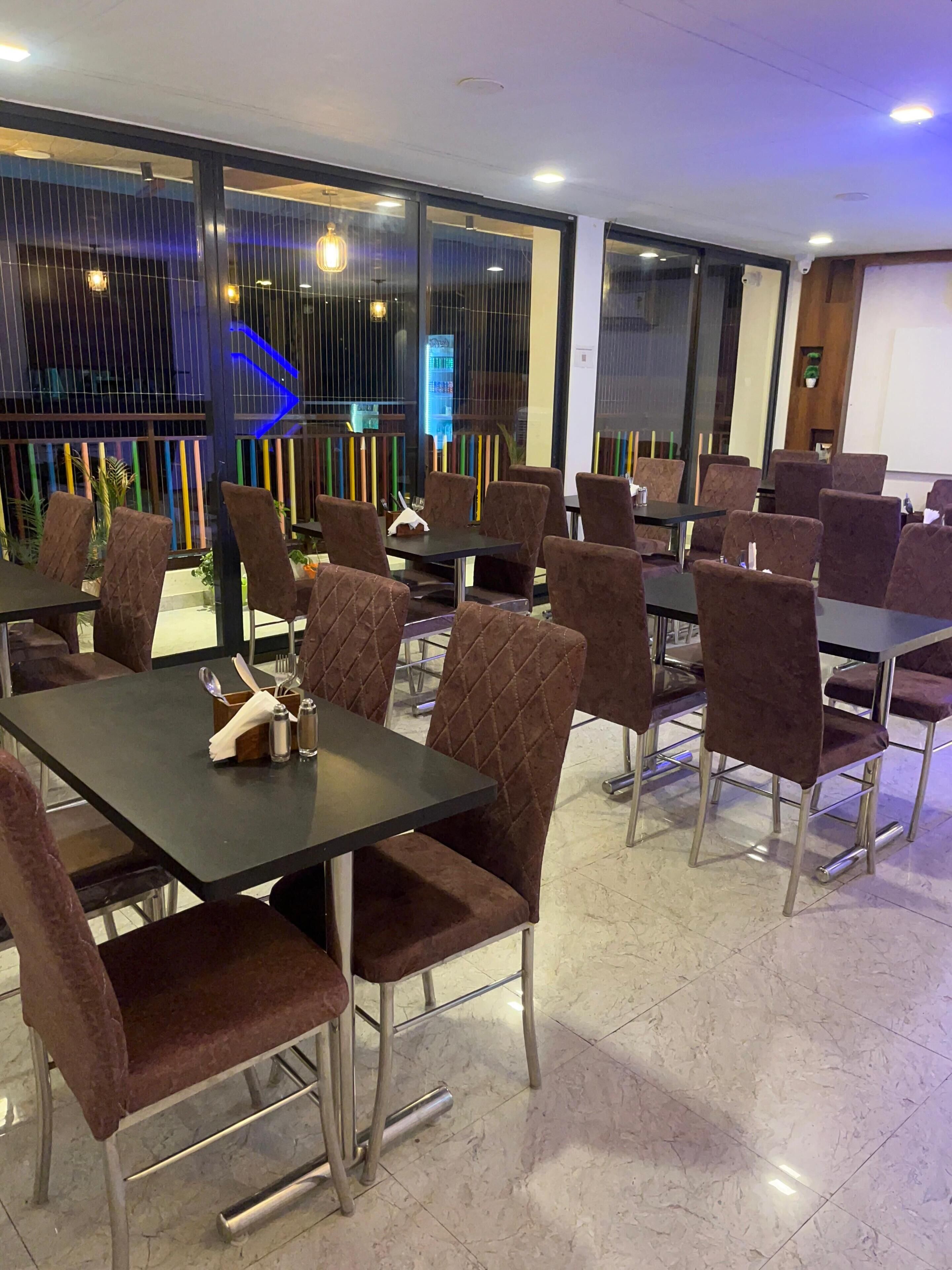 A dining area with multiple tables and chairs, large windows with a view, and a modern interior design.