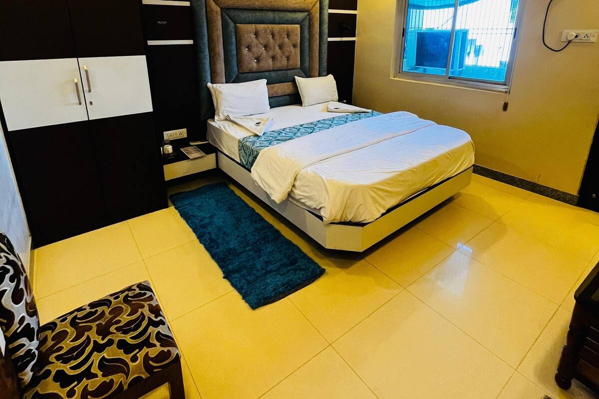 A bedroom with a bed, a ceiling fan, an air conditioning unit, a window, and a chair.
