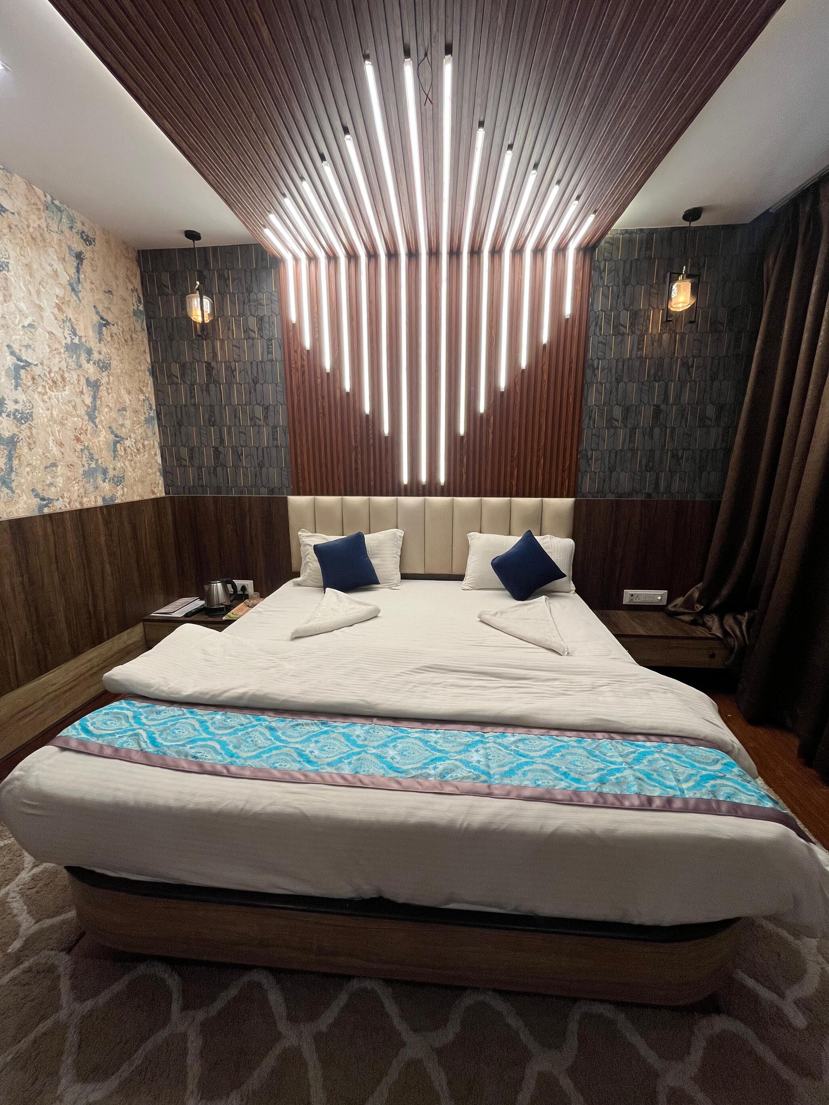 A modern hotel room with a large bed, wooden panel ceiling, and patterned wall tiles.