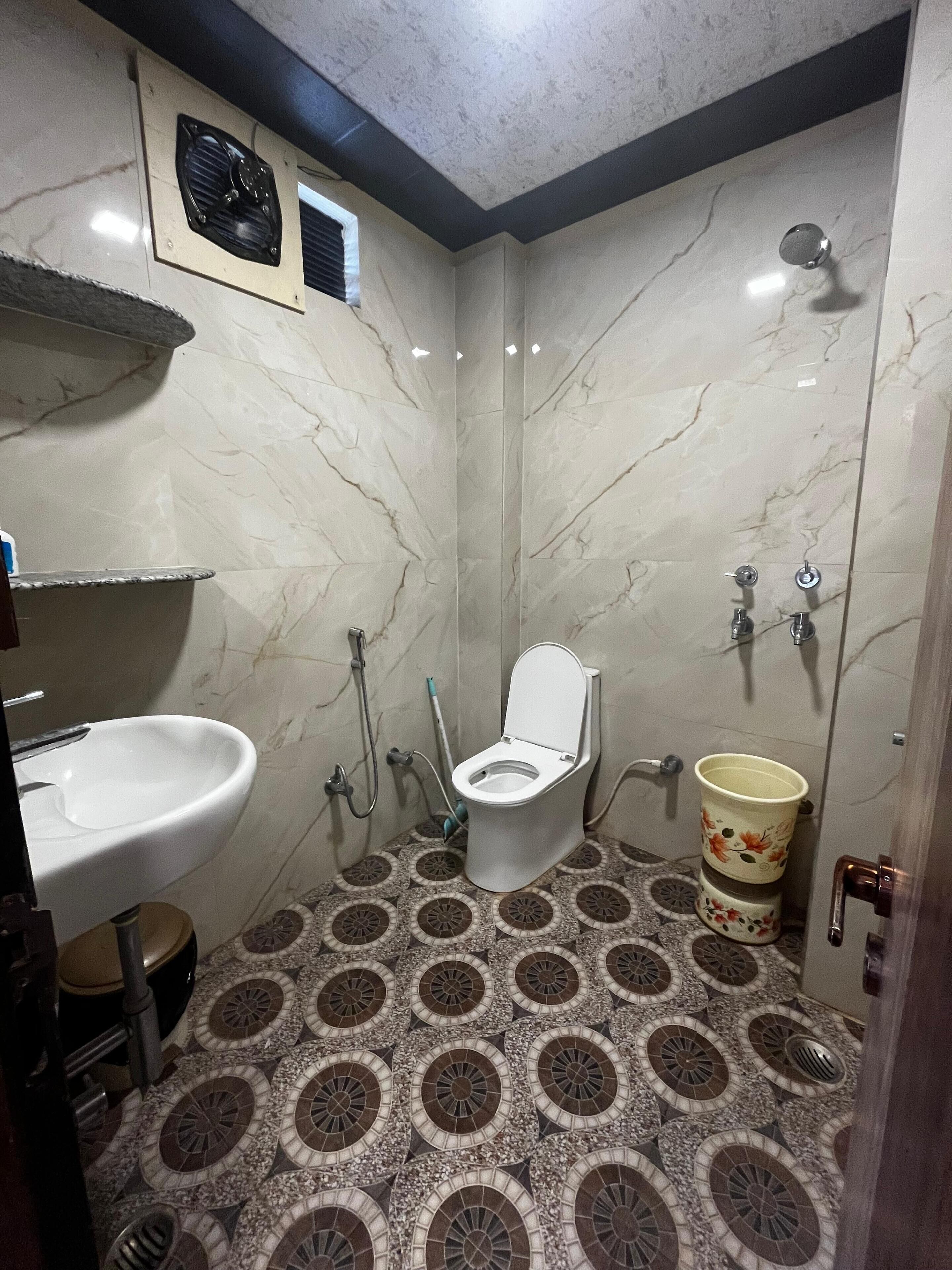 Un baño con inodoro, lavabo y ducha. El suelo presenta un diseño de baldosas estampadas.