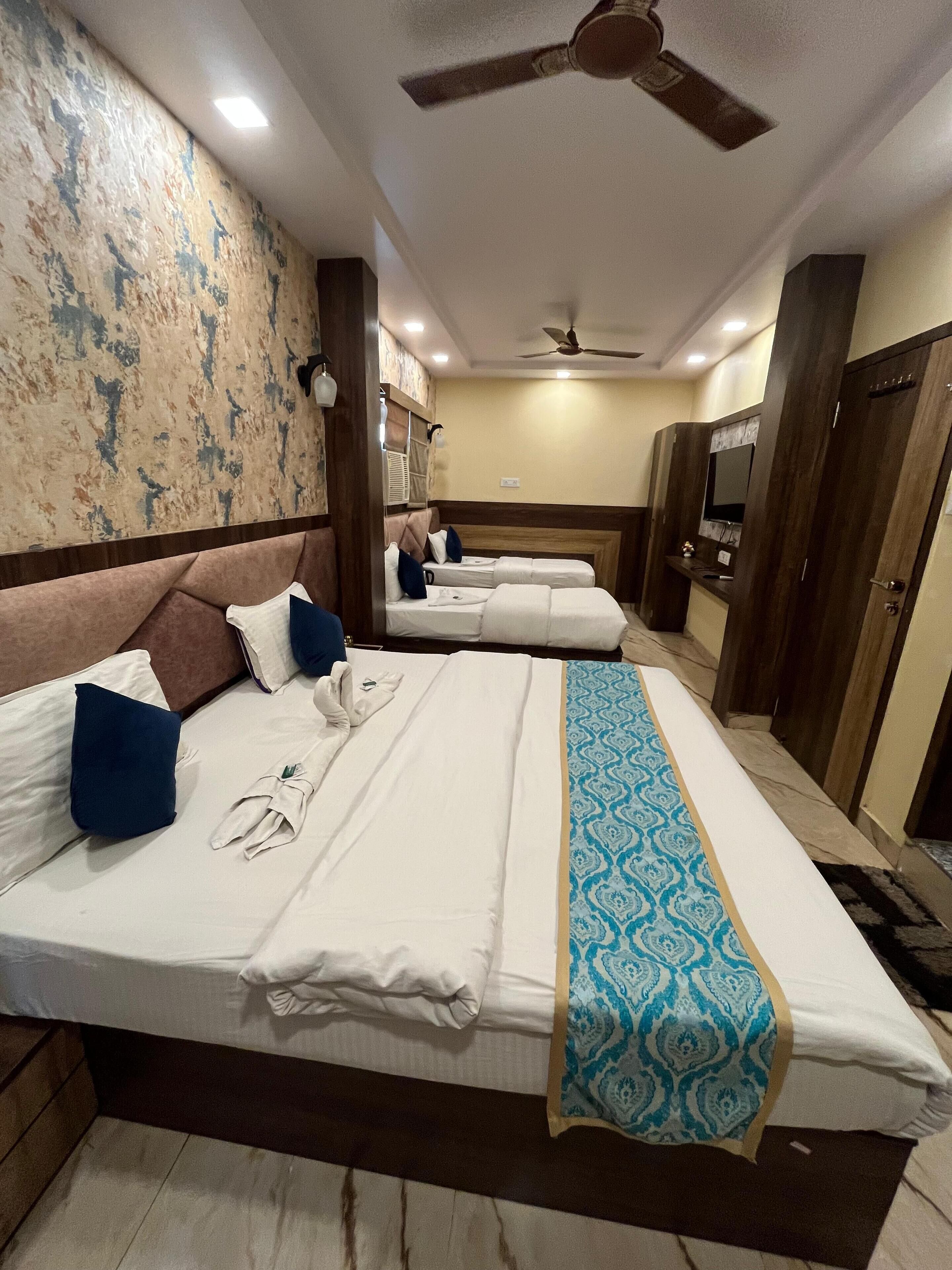 Une chambre d’hôtel avec deux lits, un ventilateur de plafond, une télévision et un couvre-lit à motifs.