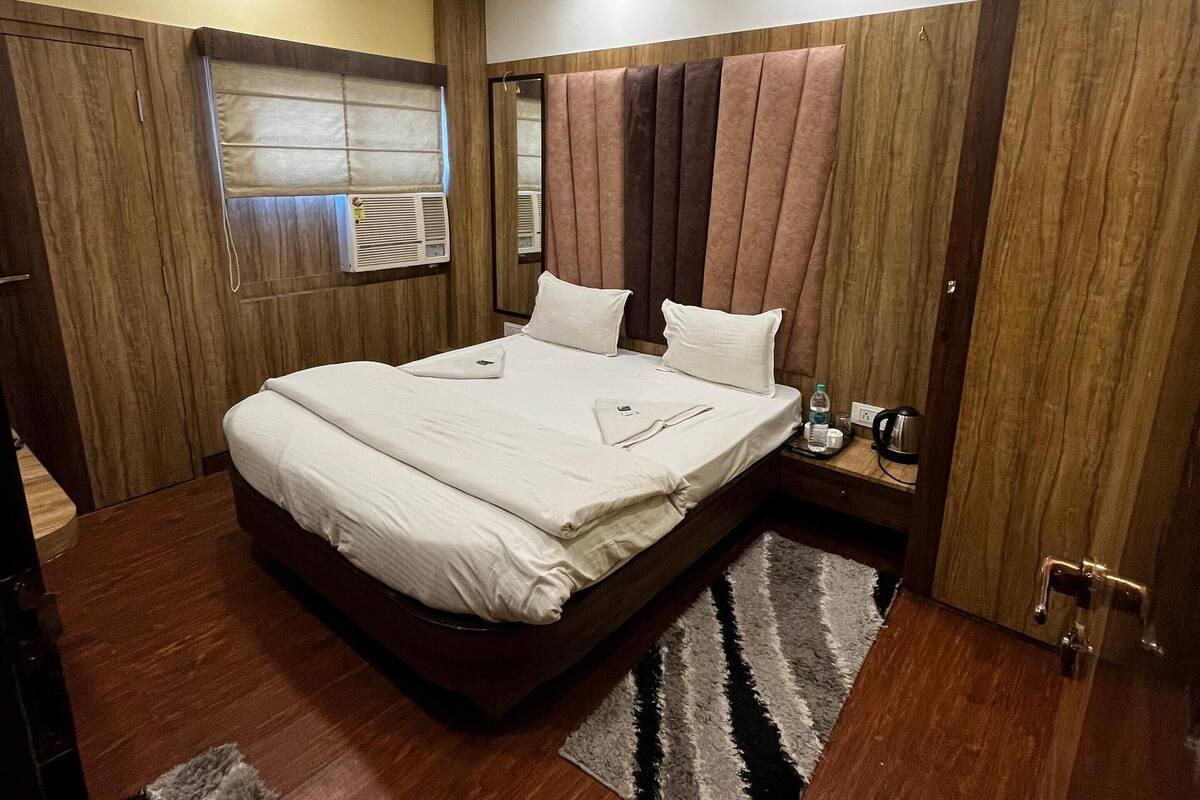 A bedroom with a bed, a ceiling fan, a window with blinds, a wooden wardrobe, and a nightstand with a lamp.
