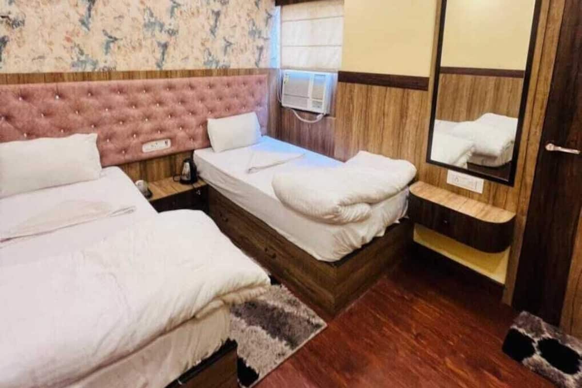 A hotel room with two beds, a ceiling fan, a wooden headboard, a mirror, and a small bench.
