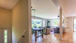 Un vaste espace de vie doté d’un plancher en bois, d’une table à manger avec des chaises, d’un canapé et offrant une vue sur la verdure environnante.