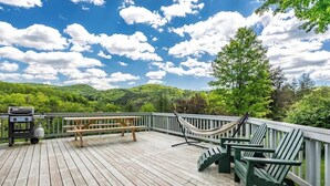 Une terrasse en bois équipée d’un barbecue, d’une table de pique-nique et de chaises Adirondack.