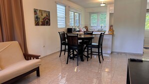 A dining area with a table and chairs, a sofa, and a kitchen in the background. - First Floor Unit with big patio. Countryside steps away from beautiful beaches. (Cabo Rojo)