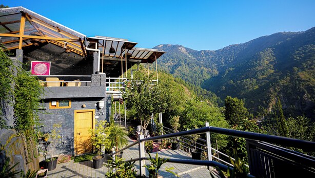 A building with a wooden balcony, potted plants, and a mountain view. - Valtara Resort (Nainital)