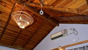 A wooden-framed room with a bed, a sofa, a wooden coffee table with fruit, and an air conditioning unit. - Valtara Resort (Nainital)