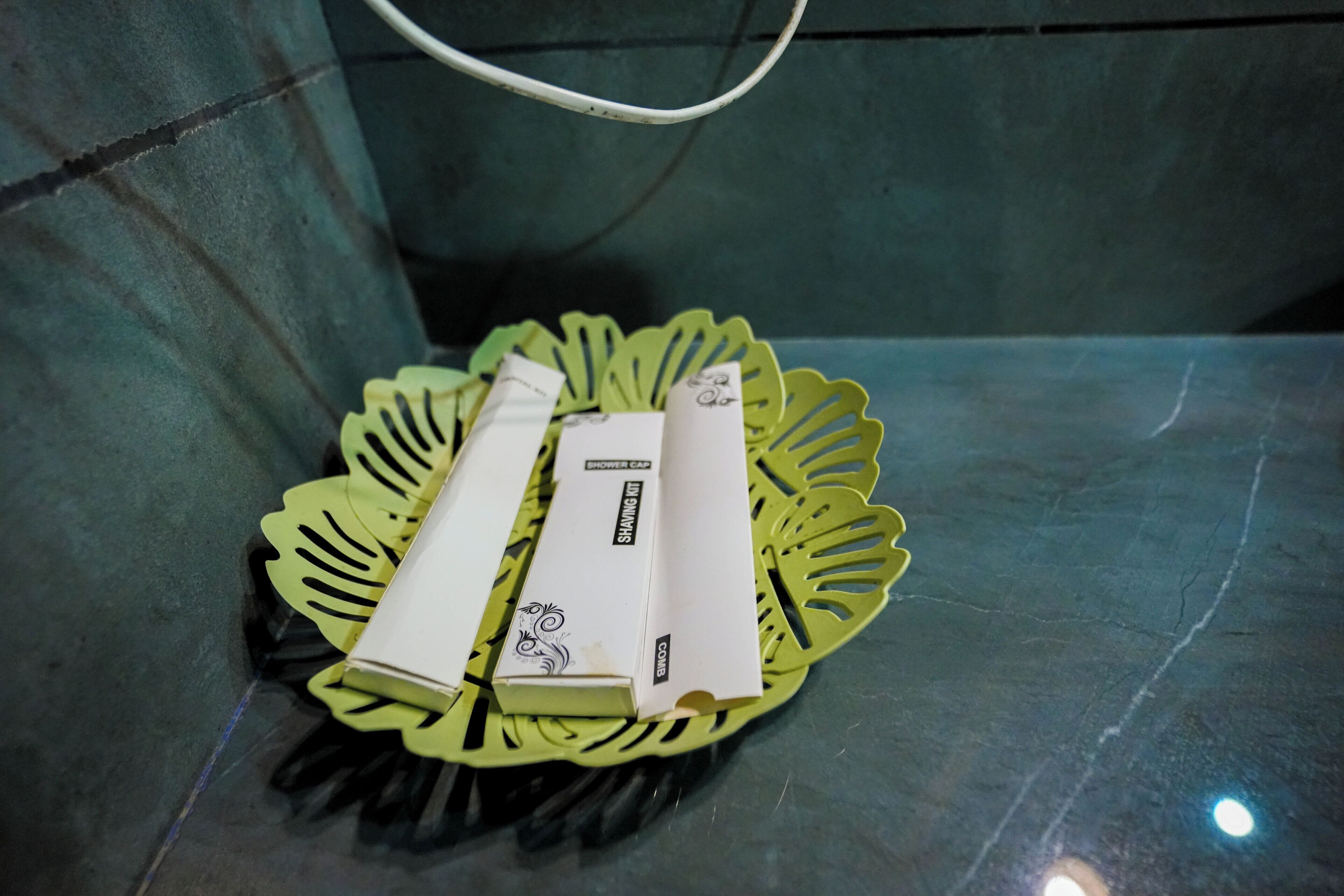 A shower cap and razor on a green leaf-shaped tray on a bathroom counter.