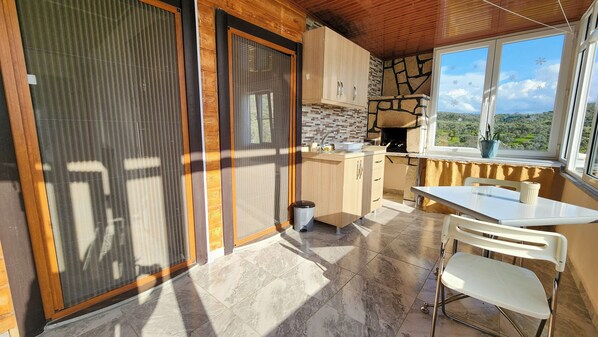 A kitchen with a stone backsplash, a window overlooking a landscape, and a dining area with a table and chairs.