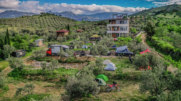 Un paisaje montañoso con un edificio, tiendas de campaña y vehículos estacionados.