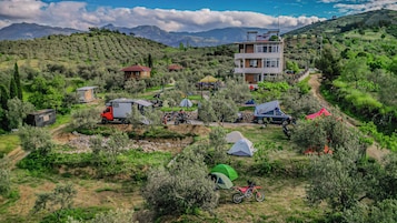 Un paisaje montañoso con un edificio, tiendas de campaña y vehículos estacionados.