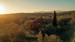A wooden cabin with a red roof surrounded by dense shrubbery and trees, set against a backdrop of hills. - Oli Kazdaglari (Edremit)