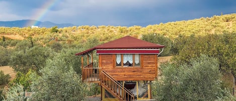 A wooden cabin with a red roof, a balcony, and a table with chairs in front.