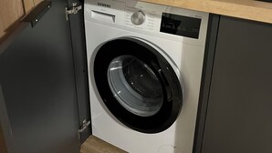 Une cuisine compacte équipée d’un lave-linge Siemens, d’une machine à café et d’un petit plan de travail.