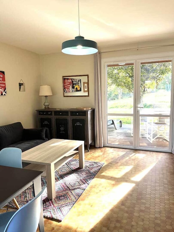 A living room with a sofa, a coffee table, a lamp, a cabinet, and a large window with a view of greenery.