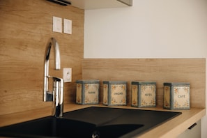 A kitchen with a modern faucet, wooden wall paneling, and a shelf with five vintage-style tin containers labeled with food items.
