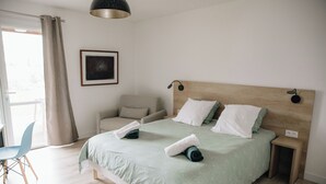 Une chambre à coucher bien rangée, avec un lit, une chaise, une table de chevet et une lampe fixée au mur.