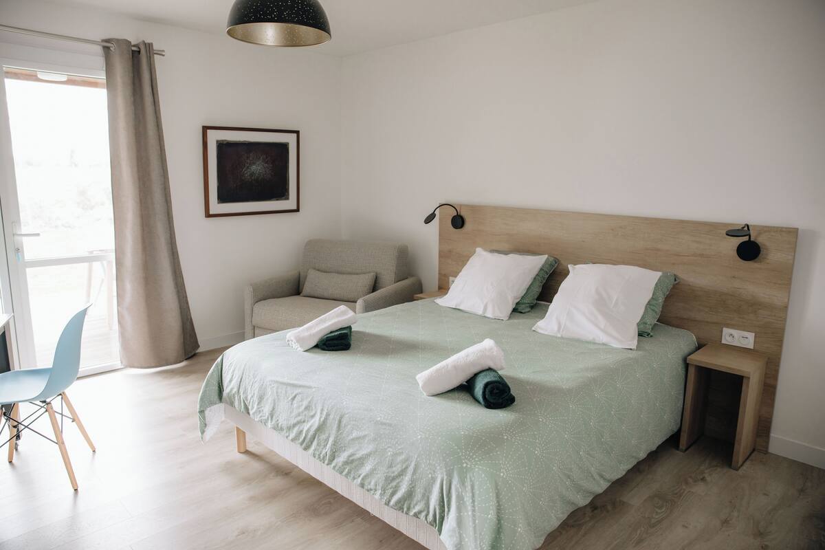 A neatly arranged bedroom with a bed, a chair, a bedside table, and a wall-mounted lamp.