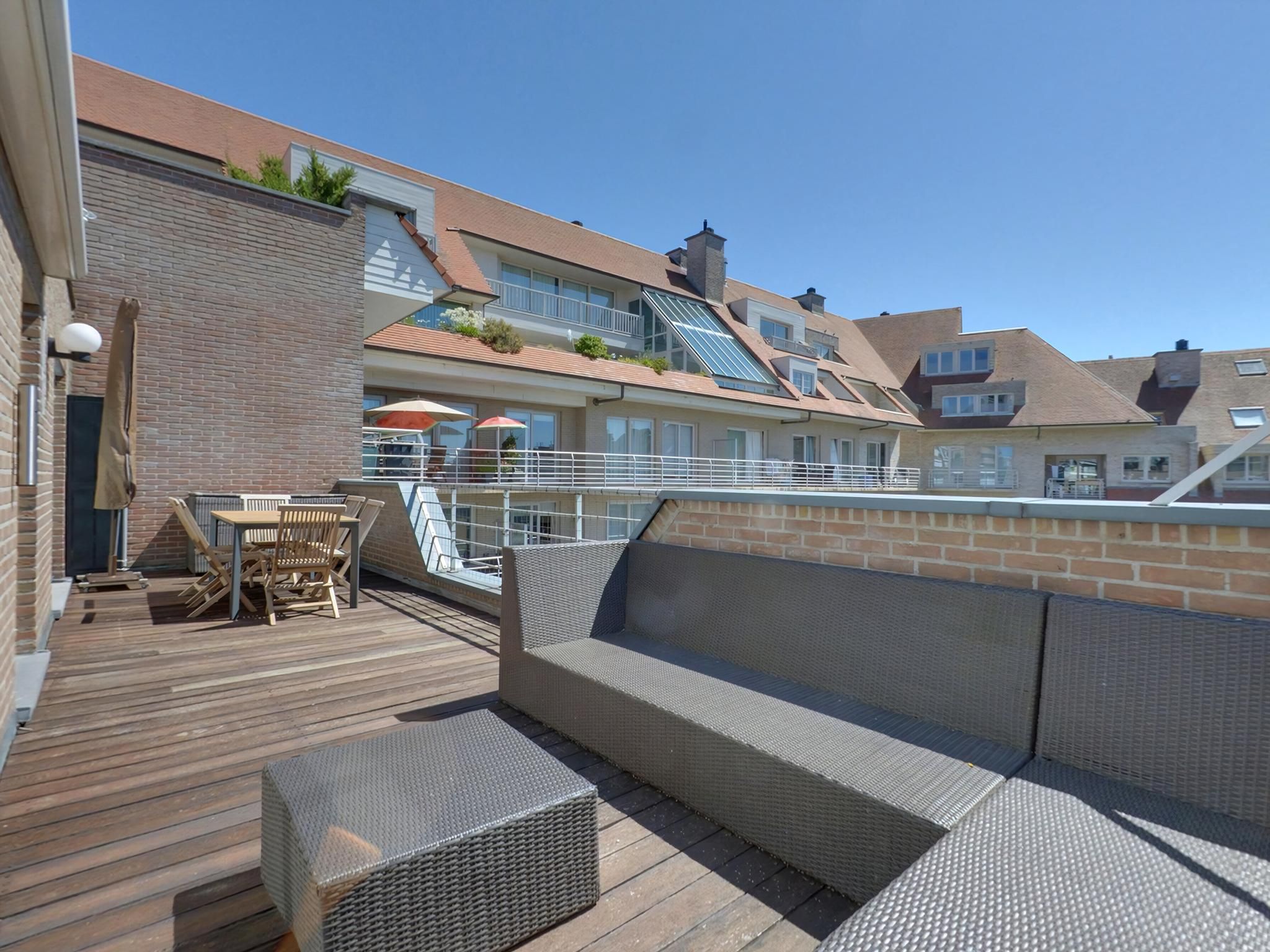 Een terras met buitenmeubilair, een hekwerk en uitzicht op omliggende gebouwen.