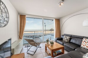 Ein modernes Wohnzimmer mit einer Ledersofa, einem Holztisch und einem großen Fenster mit Blick auf den Strand.