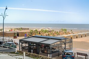 A coastal view with beach huts, a restaurant, and a car parked on the side. - 1 bedroom accommodation in Blankenberge (Blankenberge)