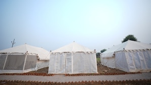 A row of white tents with a flat roof, arranged in a line on a gravel surface. - Van Bagh Camp Village (Alwar)