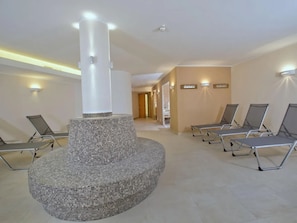 Un área de espera moderna con una estructura de mosaico central, múltiples sillones de descanso e iluminación empotrada en la pared.