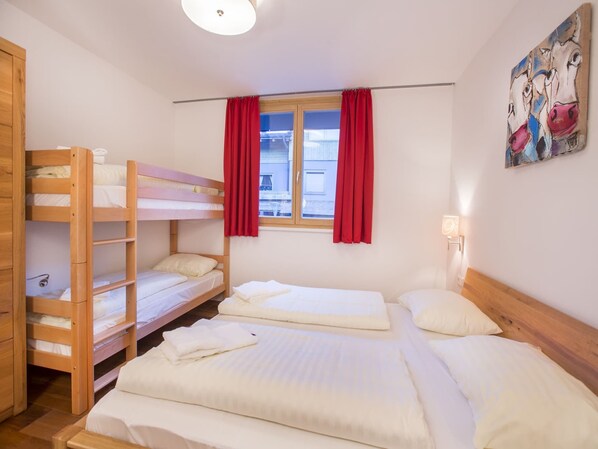 Ein Zimmer mit Etagenbetten, einem Fenster mit roten Vorhängen, einem Bild an der Wand und einer Nachttischlampe.
