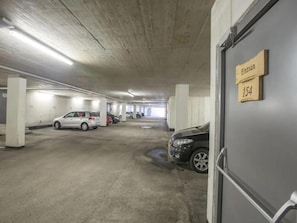 A parking garage with concrete pillars, a white car, and a black car parked.