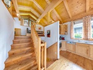 A wooden interior with a staircase, kitchen, and a window with curtains.