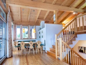 A wooden interior with a dining area, staircase, and large windows.