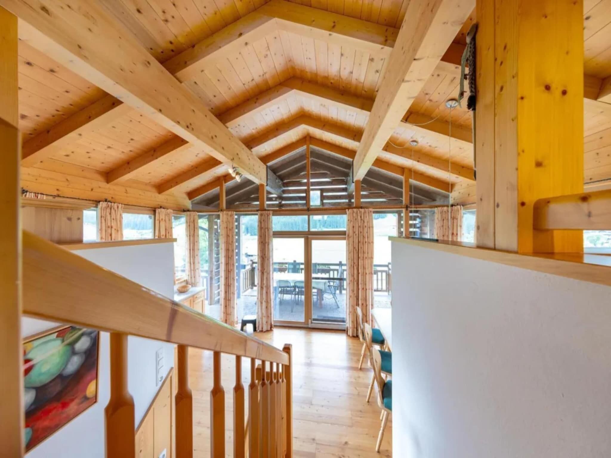 A wooden interior with a high ceiling, a staircase, and large windows.