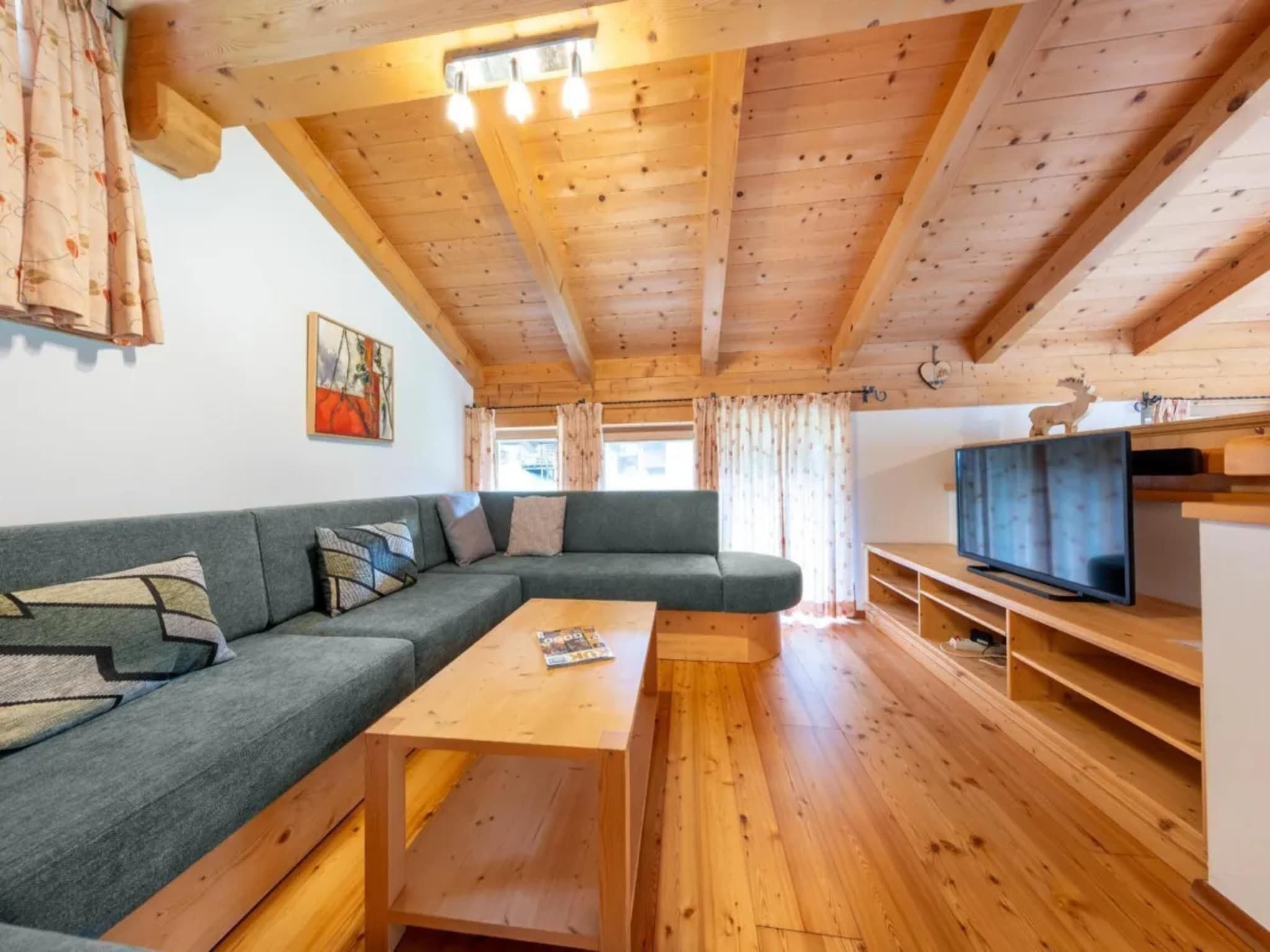 Ein gemütliches Wohnzimmer mit einem Ecksofa, einem Holztisch und einem Fernseher auf einem Holzboden.