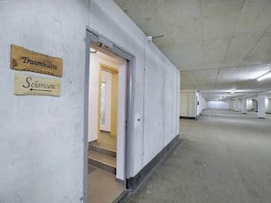 A long, empty corridor with a door leading to a room with a bed and a window. There are signs on the wall indicating 'Traumhütte' and 'Schiraum.'