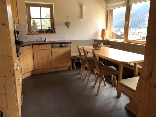 A kitchen with wooden cabinets, a dishwasher, a window with a view of mountains, and a dining area with a table and chairs.