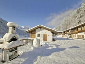 Ein mit Schnee bedecktes Berghotel mit Holzfassade und einem zentralen Gebäude mit einer braunen Tür.