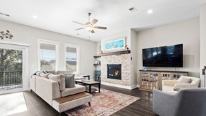 A modern living room with a fireplace, a flat-screen TV, and a ceiling fan.
