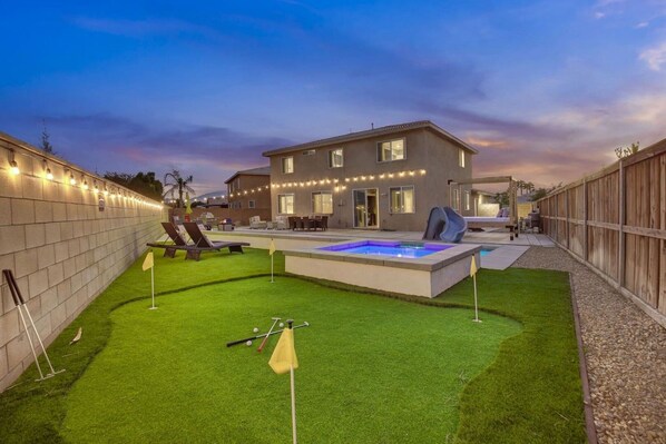 A backyard with artificial grass, a hot tub, and a pool.