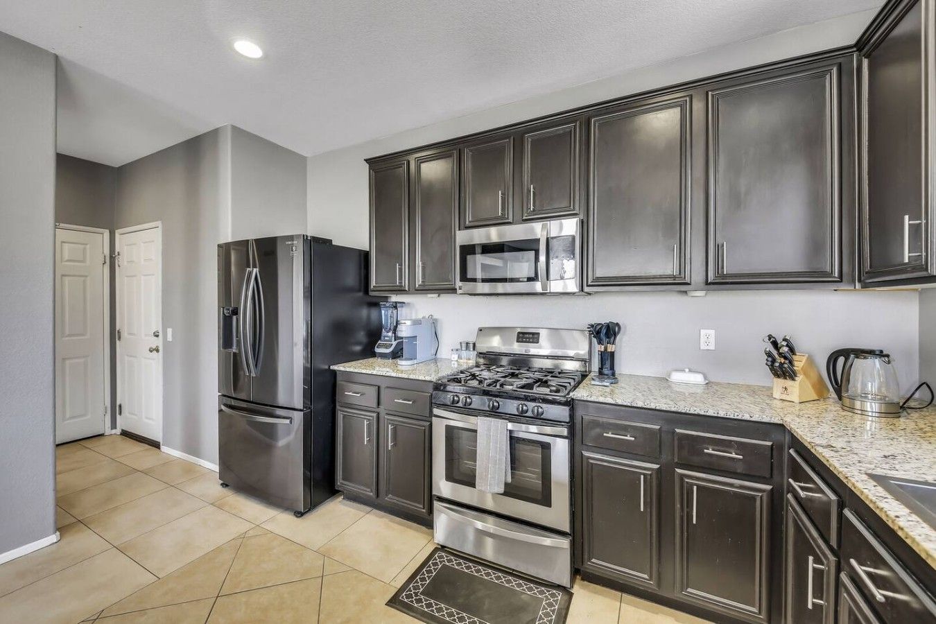 A kitchen with dark cabinets, stainless steel appliances, a microwave, and a gas stove.