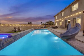 A swimming pool with a slide, lounge chairs, and a patio area with outdoor seating.
