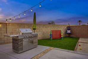 Un espace barbecue extérieur équipé d’un gril, de guirlandes lumineuses et d’une structure de jeux pour enfants.