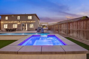 A backyard with a swimming pool, a slide, a deck with outdoor furniture, and a wooden fence. - Wonders Nest: Pool, Spa, Arcades, Putting Green! (Coachella)