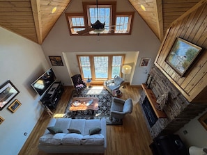 A spacious living area with a high ceiling, wooden beams, a fireplace, and large windows.