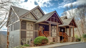 A large, multi-story house with a prominent front porch, stone foundation, and a steeply pitched roof.